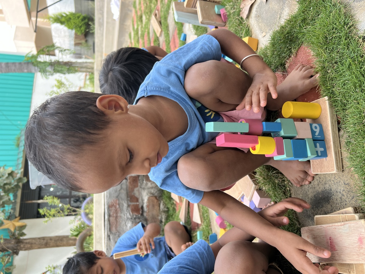 A child carefully balancing a tall tower of colourful wooden blocks on the grass
