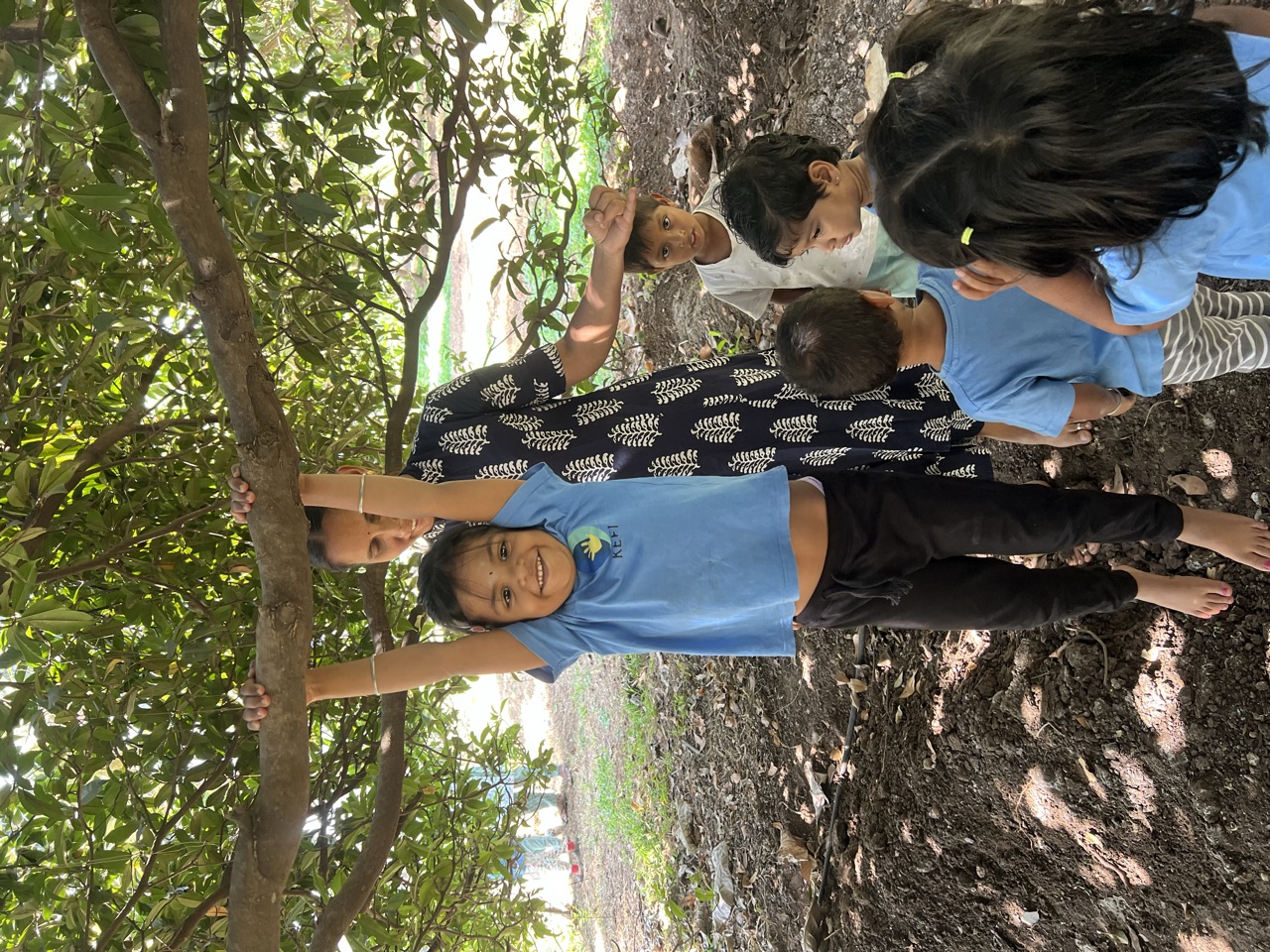 A child swinging from a low branch while a teacher and friends look on