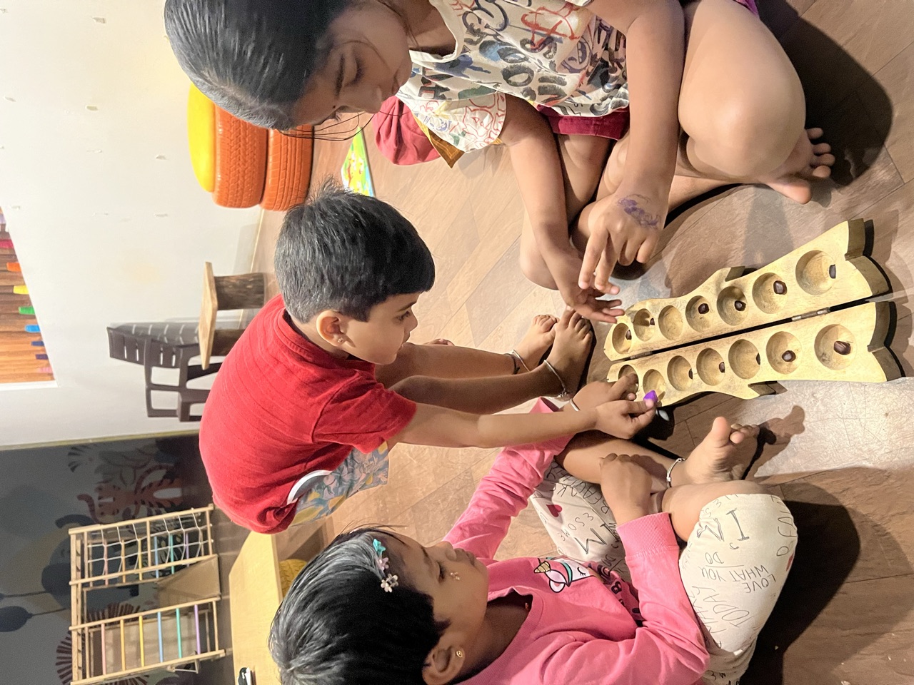 Three children playing a wooden counting game together on the floor