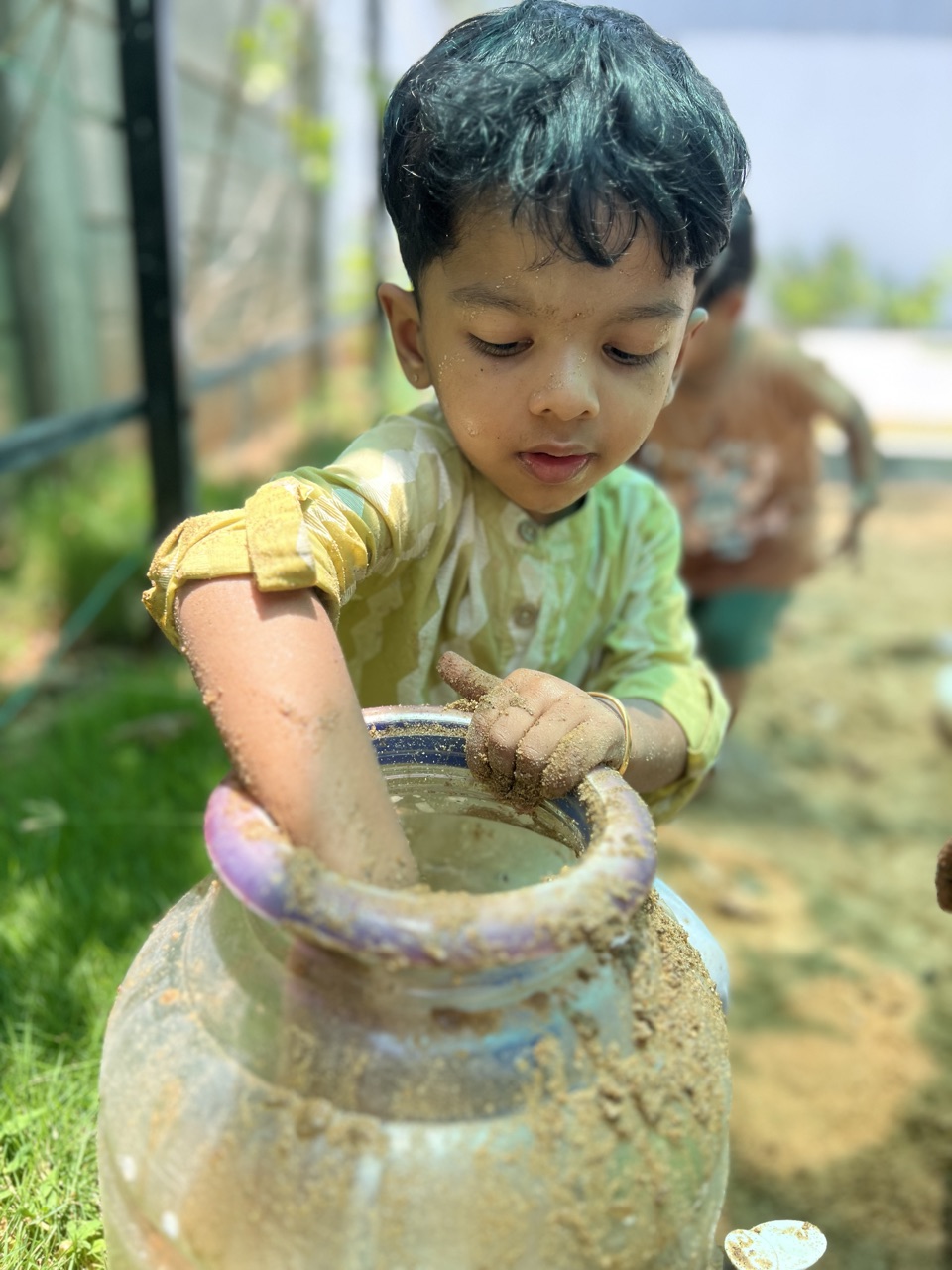 A child with sandy hands exploring at a clay pot during sensory play