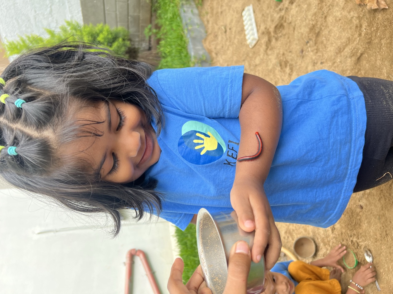 A smiling child letting a little earthworm crawl up her arm