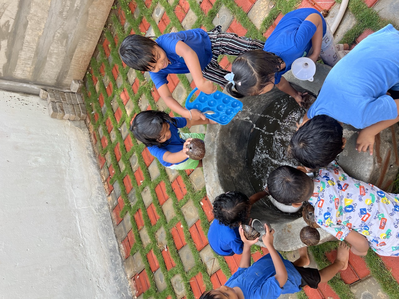 Children scooping and splashing water together inside a big stone well