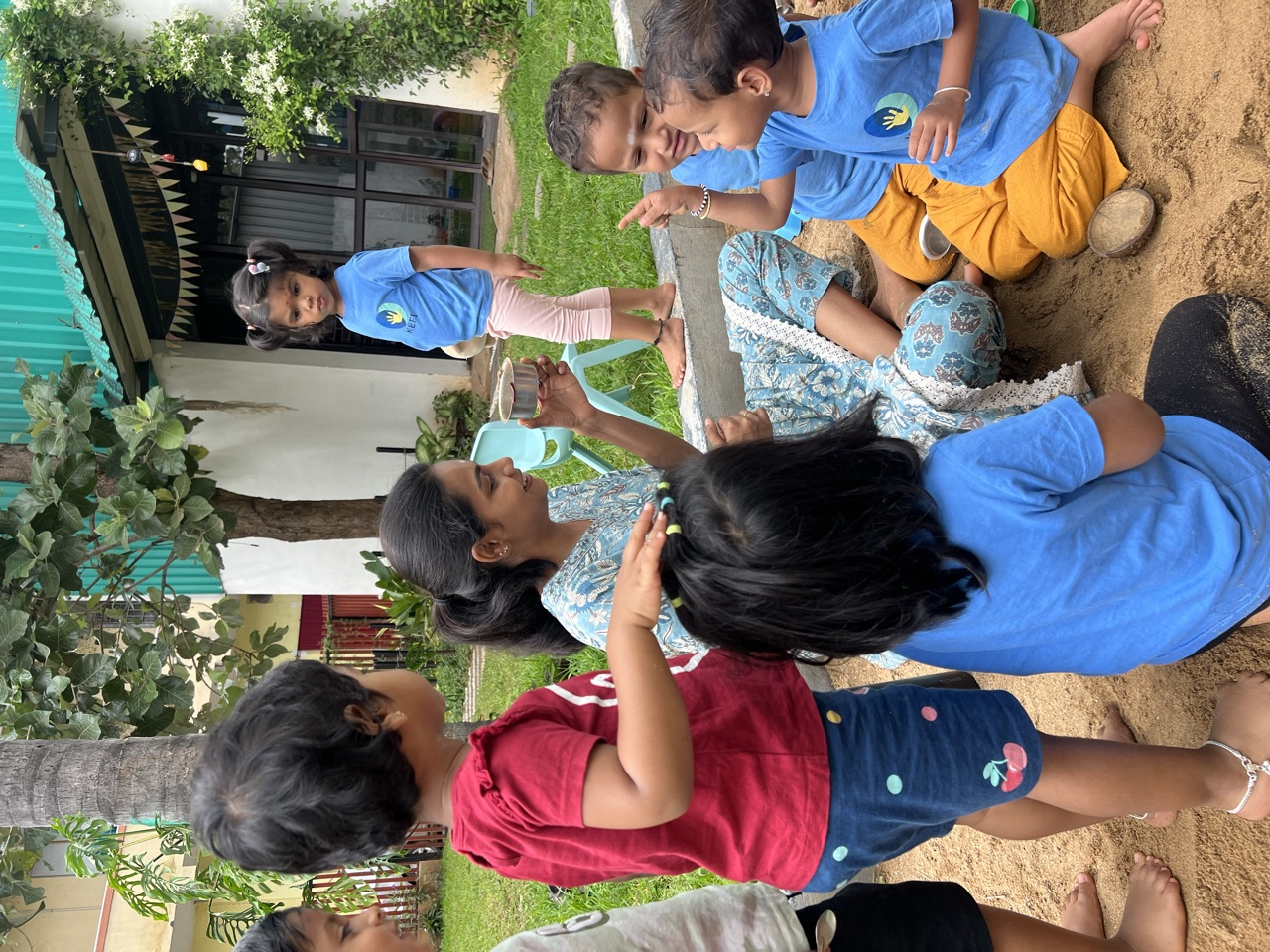 Children gathered around their teacher in the sandpit, peering into a glass jar