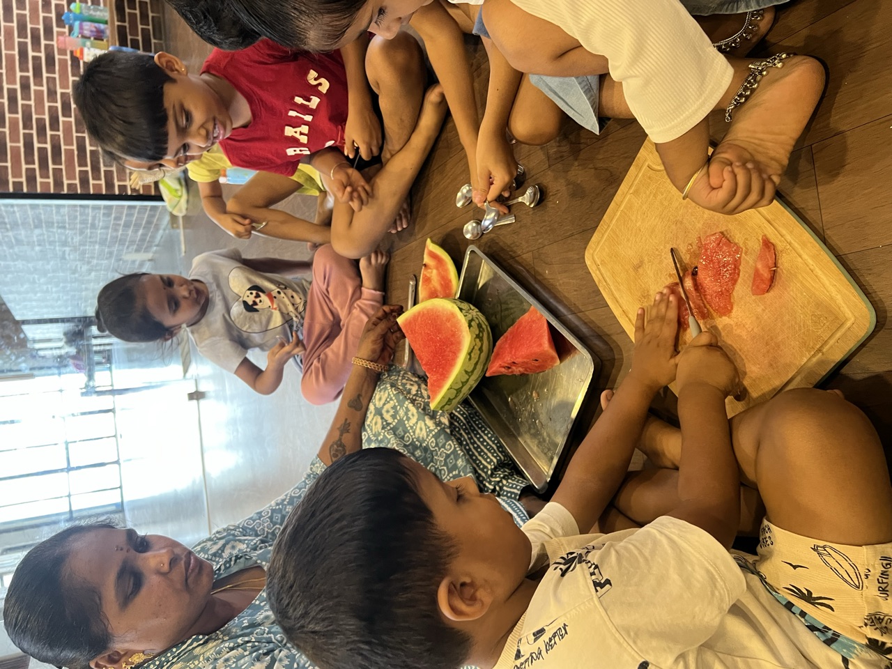 Children slicing watermelon together on a wooden board with their teacher
